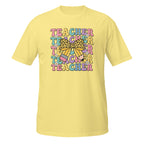 A pale yellow short-sleeve t-shirt with a colorful retro-style graphic on the chest that reads 'TEACHER TEACHER TEACHER' in pastel letters, decorated with a bow and pencil illustration.