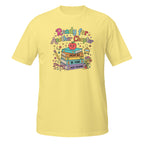 A light yellow short-sleeve t-shirt with a colorful graphic on the chest that reads 'Ready for Another Chapter' above a stack of books, a smiling apple, and school-themed illustrations.