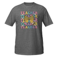 A heather gray short-sleeve t-shirt with a colorful retro graphic on the chest that reads 'TEACHER' repeated in pastel letters, overlaid with a yellow leopard-print bow and small pink and blue pencil illustrations, shown on a plain white background.