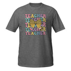 A heather gray short-sleeve t-shirt with a colorful retro graphic on the chest that reads 'TEACHER' repeated in pastel letters, overlaid with a yellow leopard-print bow and small pink and blue pencil illustrations, shown on a plain white background.