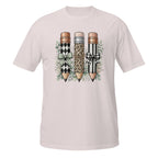 A light pink short-sleeve crewneck t-shirt featuring a graphic print of three decorative pencils with leopard, harlequin, and black-and-white striped patterns, accented with bows and green leaves.