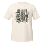 An off-white short-sleeve t-shirt with a graphic print of three decorative pencils (one with a black and white harlequin pattern, one with a leopard print, and one with a black and white striped pattern) adorned with bows and green leaves, displayed on a solid white background.