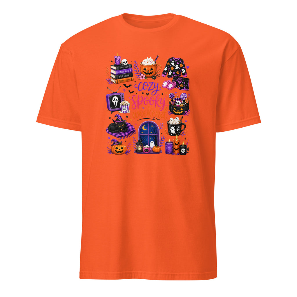An orange short-sleeve crewneck t-shirt featuring a colorful graphic print on the front with various cute Halloween-themed illustrations, including pumpkins, a ghost, a mug, and a window, with the text 'Cozy Happy Halloween'.