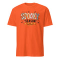 An orange short-sleeve crewneck t-shirt featuring a 'Spooky Season' graphic on the chest with Halloween-themed patterns and illustrations.
