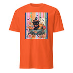 An orange short-sleeve crewneck t-shirt featuring a colorful Halloween-themed graphic print on the chest. The print depicts a black cat dressed as a witch in a cart with pumpkins, a white ghost, a moon, and bats against a striped background.