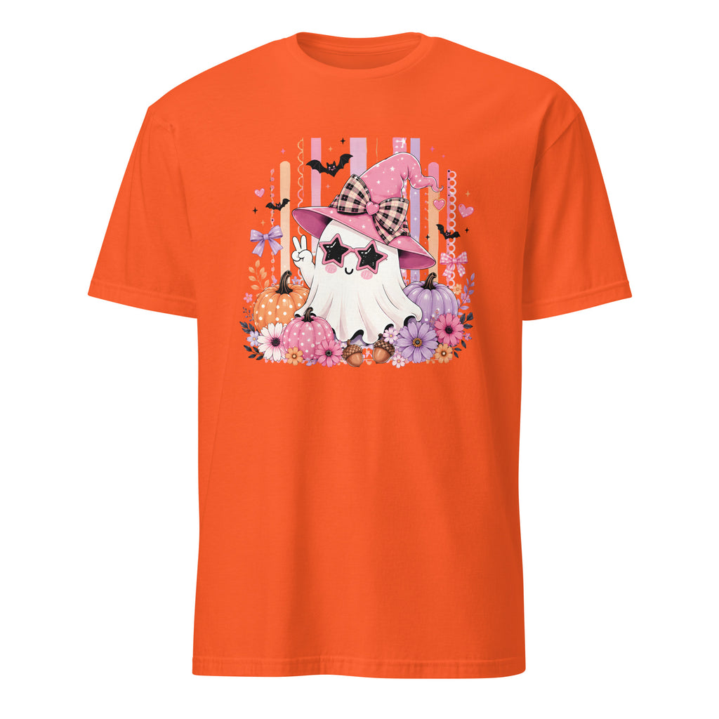An orange short-sleeve crewneck t-shirt featuring a colorful graphic print of a cute cartoon ghost wearing a pink witch hat and sunglasses, surrounded by flowers, bats, and pumpkins on a white background.