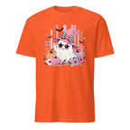 An orange short-sleeve crewneck t-shirt featuring a colorful graphic print of a cute cartoon ghost wearing a pink witch hat and sunglasses, surrounded by flowers, bats, and pumpkins on a white background.