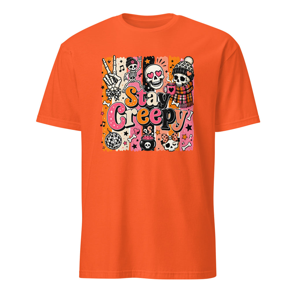 A bright orange short-sleeve crewneck t-shirt featuring a colorful graphic print on the front with the text 'Stay Creepy' and various Halloween-themed illustrations including sugar skulls, a skeleton hand, and a jack-o'-lantern.