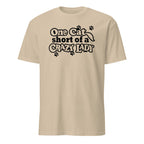 Beige t-shirt with black text 'One Cat Short of a Crazy Lady' on a white background