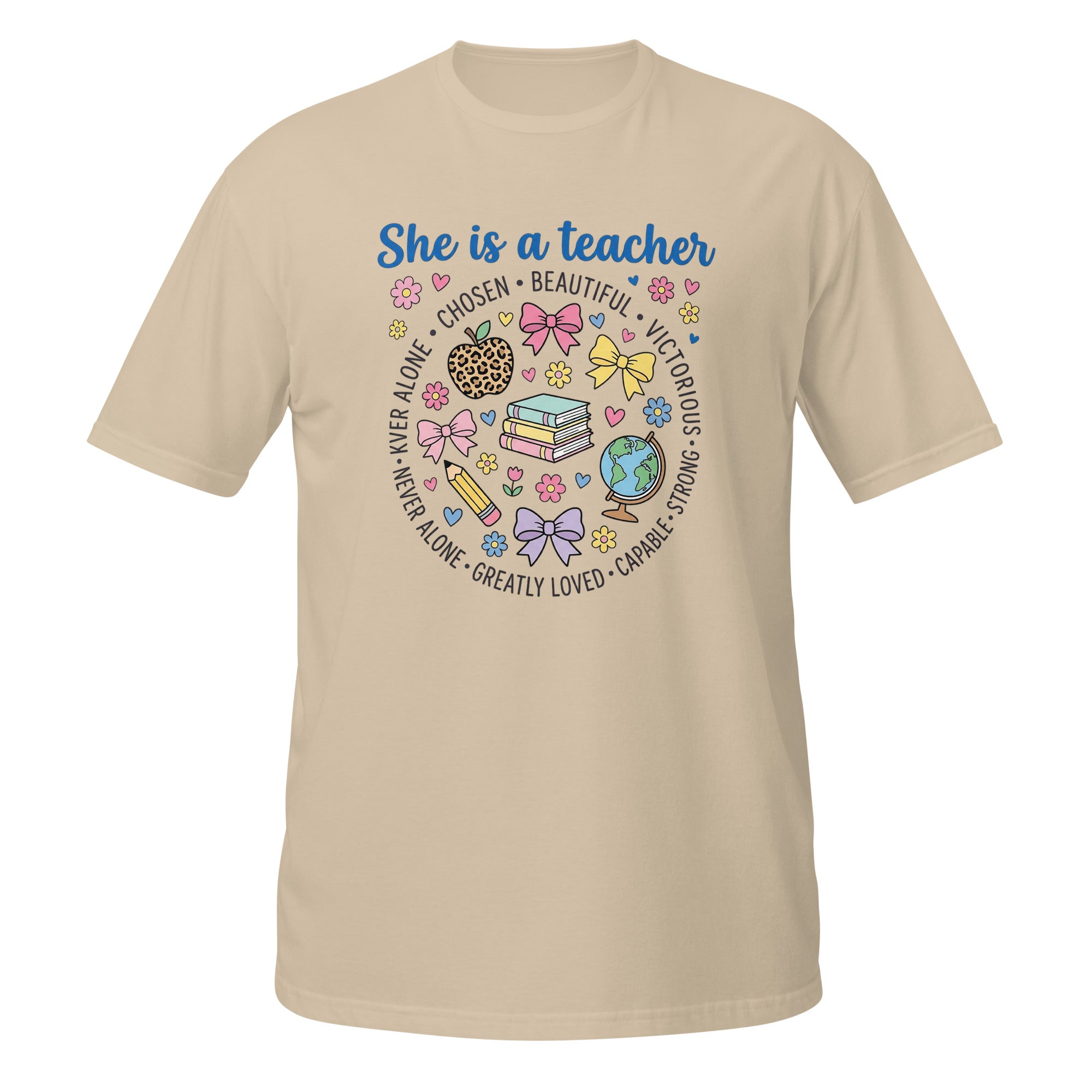A sand short-sleeve t-shirt with a colorful graphic on the front that reads 'She is a teacher' surrounded by school-themed illustrations like books, bows, a globe, and hearts.