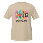 A beige short-sleeve t-shirt with a colorful 'Back to School' graphic on the chest, featuring cartoon drawings of a pencil, apple, crayon, and book over pink, blue, orange, and yellow watercolor-style stripes.