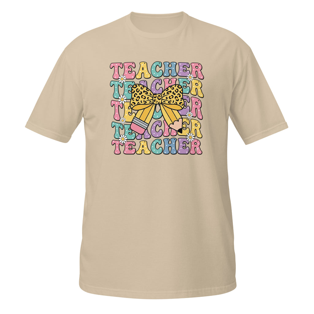 A beige short-sleeve crewneck t-shirt featuring a colorful graphic on the chest with the word 'TEACHER' repeated in pastel colors and a yellow leopard-print bow in the center.