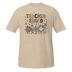 A beige short-sleeve crewneck t-shirt featuring a colorful graphic on the front that reads 'TEACHER SQUAD' above five cute cartoon characters representing school supplies and treats.