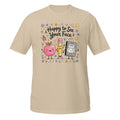 A beige short-sleeve crewneck t-shirt featuring a colorful cartoon graphic of a pink apple, a yellow pencil, and a black-and-white cat in the center, surrounded by the text 'Happy to See Your Face' and small decorative doodles.