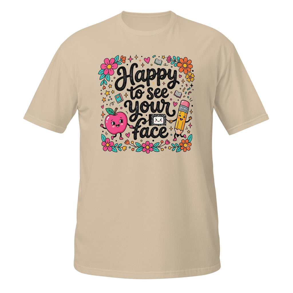 A beige short-sleeve t-shirt with a colorful graphic on the chest that reads 'Happy to see your face' in black script, surrounded by cute illustrations of a smiling pink apple, a yellow pencil, flowers, and school-themed doodles.