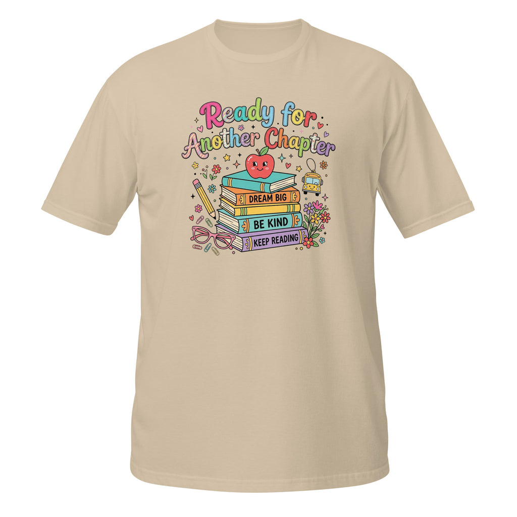 A beige short-sleeve crewneck t-shirt featuring a colorful graphic on the chest with the text 'Ready for Another Chapter' and an illustration of books, a smiling apple, and reading accessories.