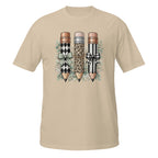 A beige short-sleeve crewneck t-shirt featuring a graphic print of three decorative pencils with diamond, leopard, and striped patterns, accented with bows and green leaves.