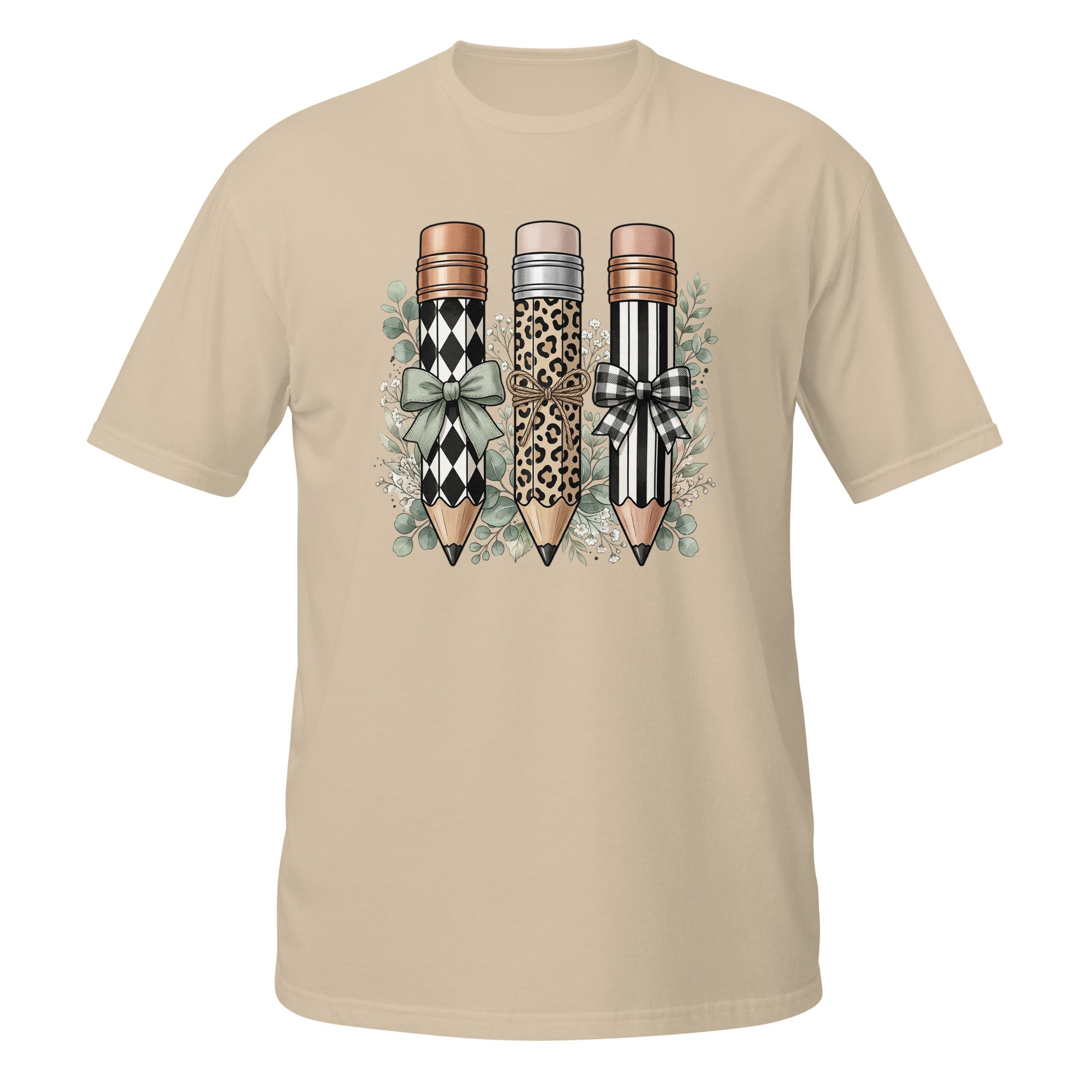 A beige short-sleeve crewneck t-shirt featuring a graphic print of three decorative pencils with diamond, leopard, and striped patterns, accented with bows and green leaves.