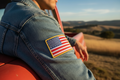 Person wearing a denim jacket with an American flag patch, sitting in a vehicle with a scenic background.